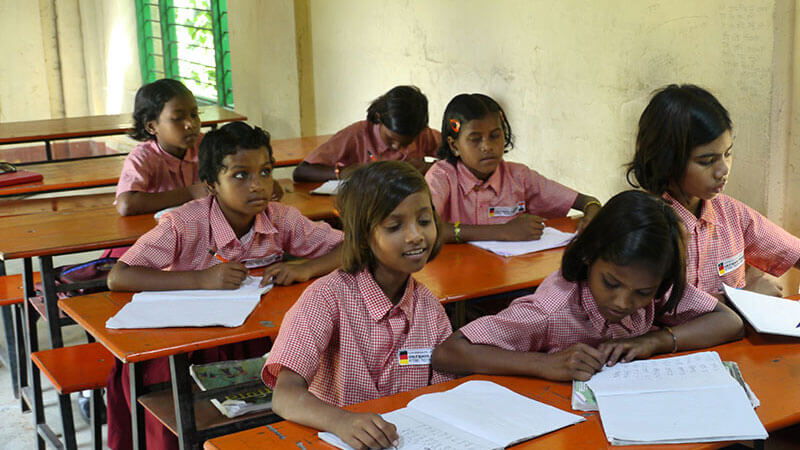 Zeigt Mädchen in Indien die in der Schule sitzen und schreiben